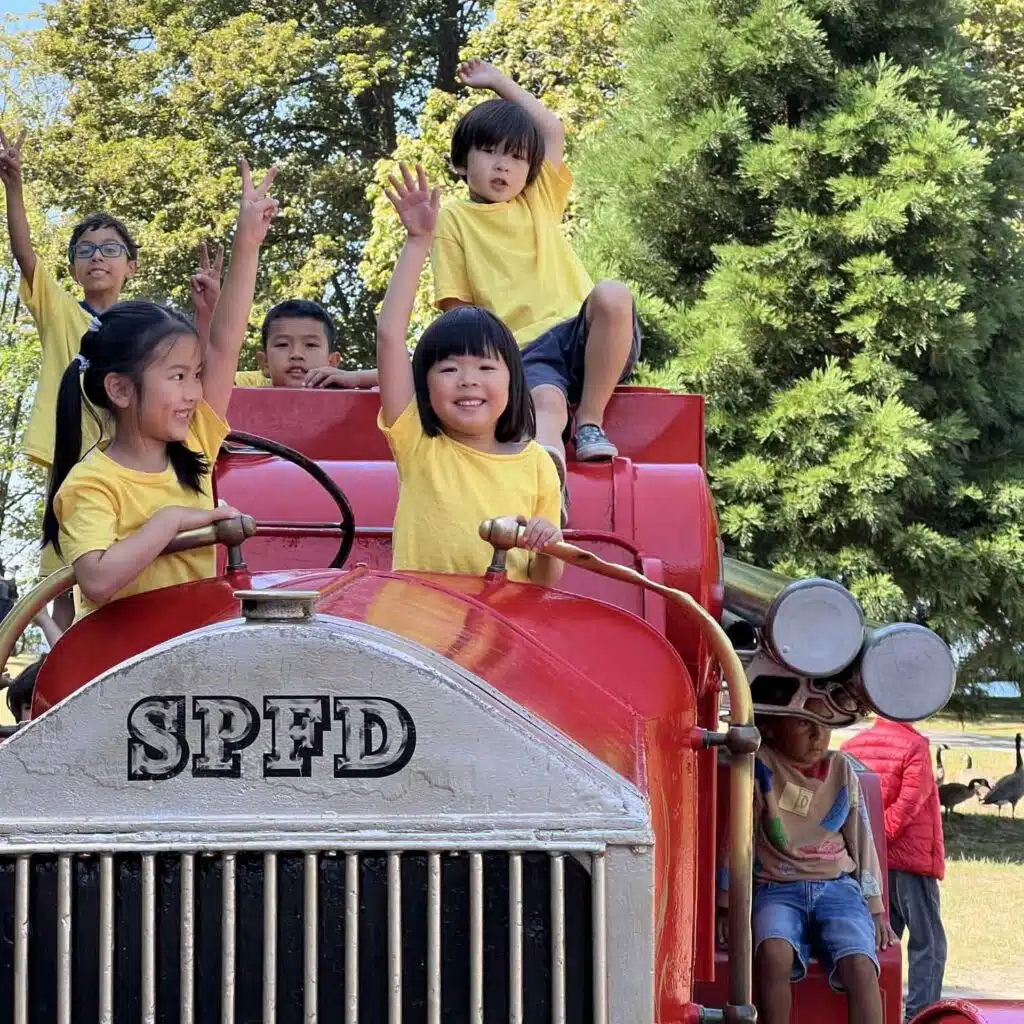Children joyfully riding on a vintage fire truck during a sunny day.
