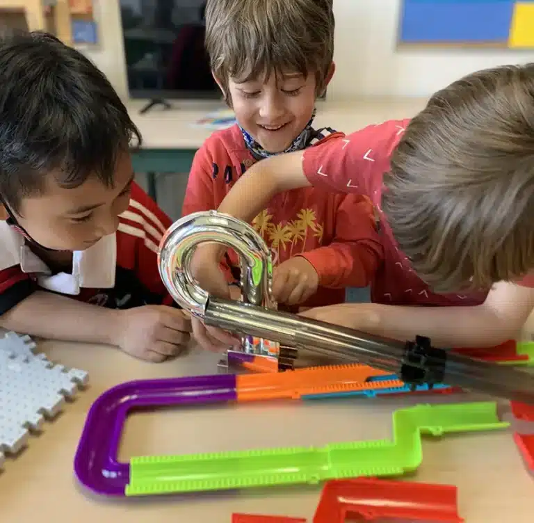 Three children intensely building a toy track together.